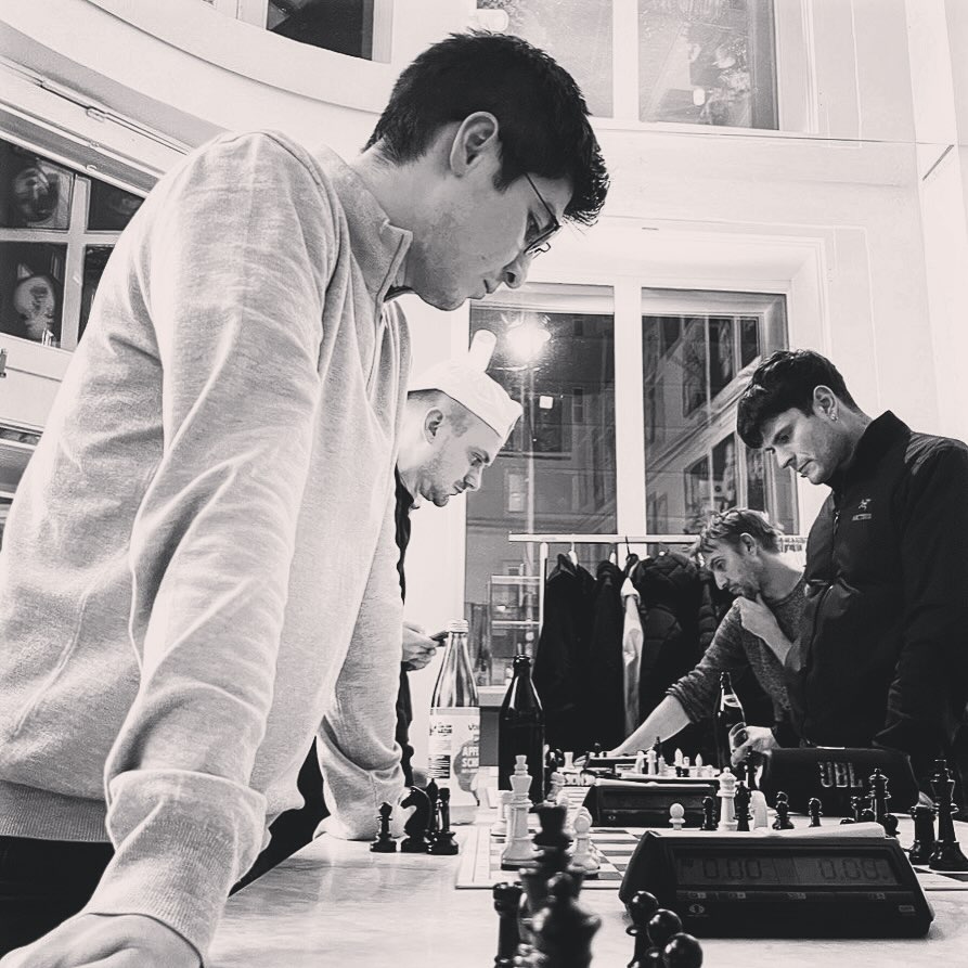 Young people standing around the counter playing chess over the board