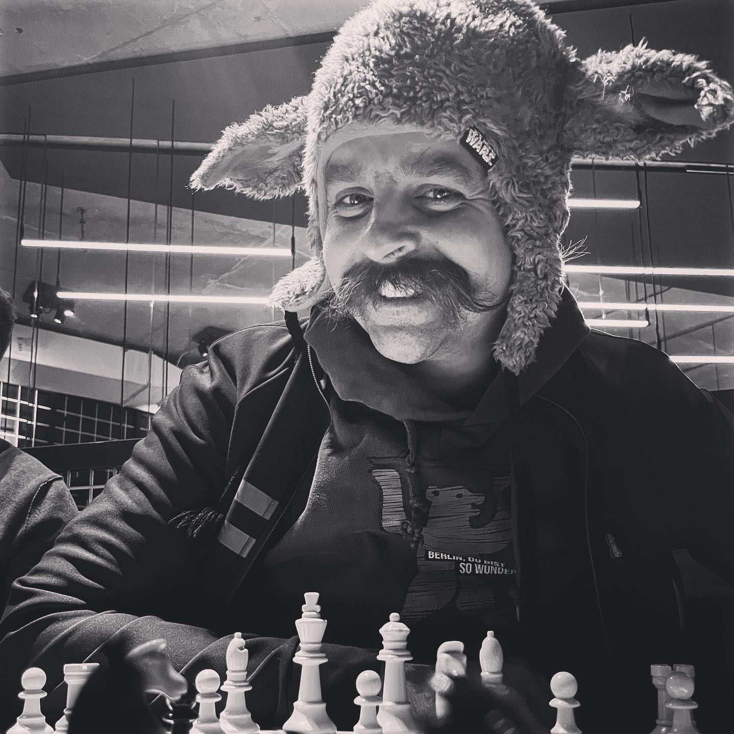 A man wearing a yoda hat sitting infront of a chessboard