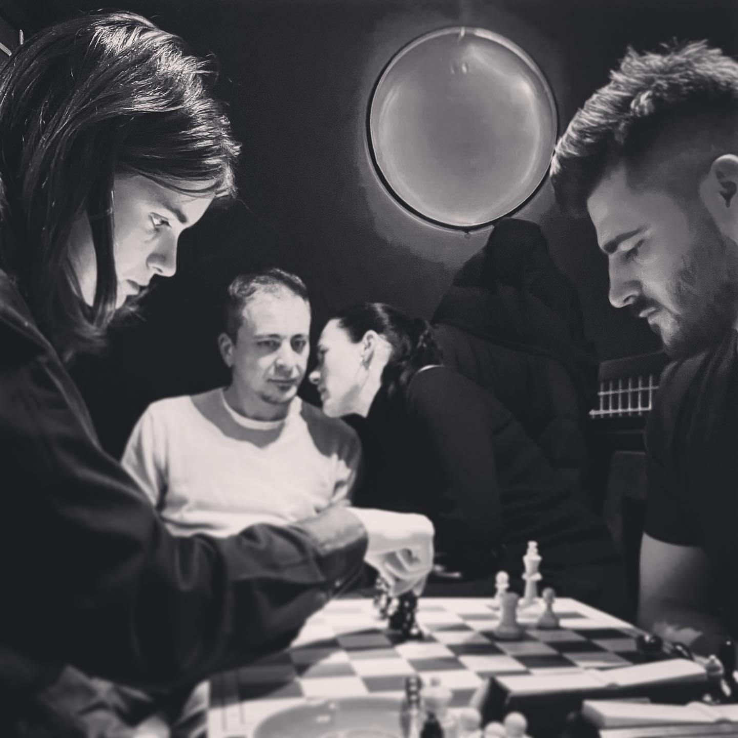 A man and a woman playing chess, a couple chatting in the background